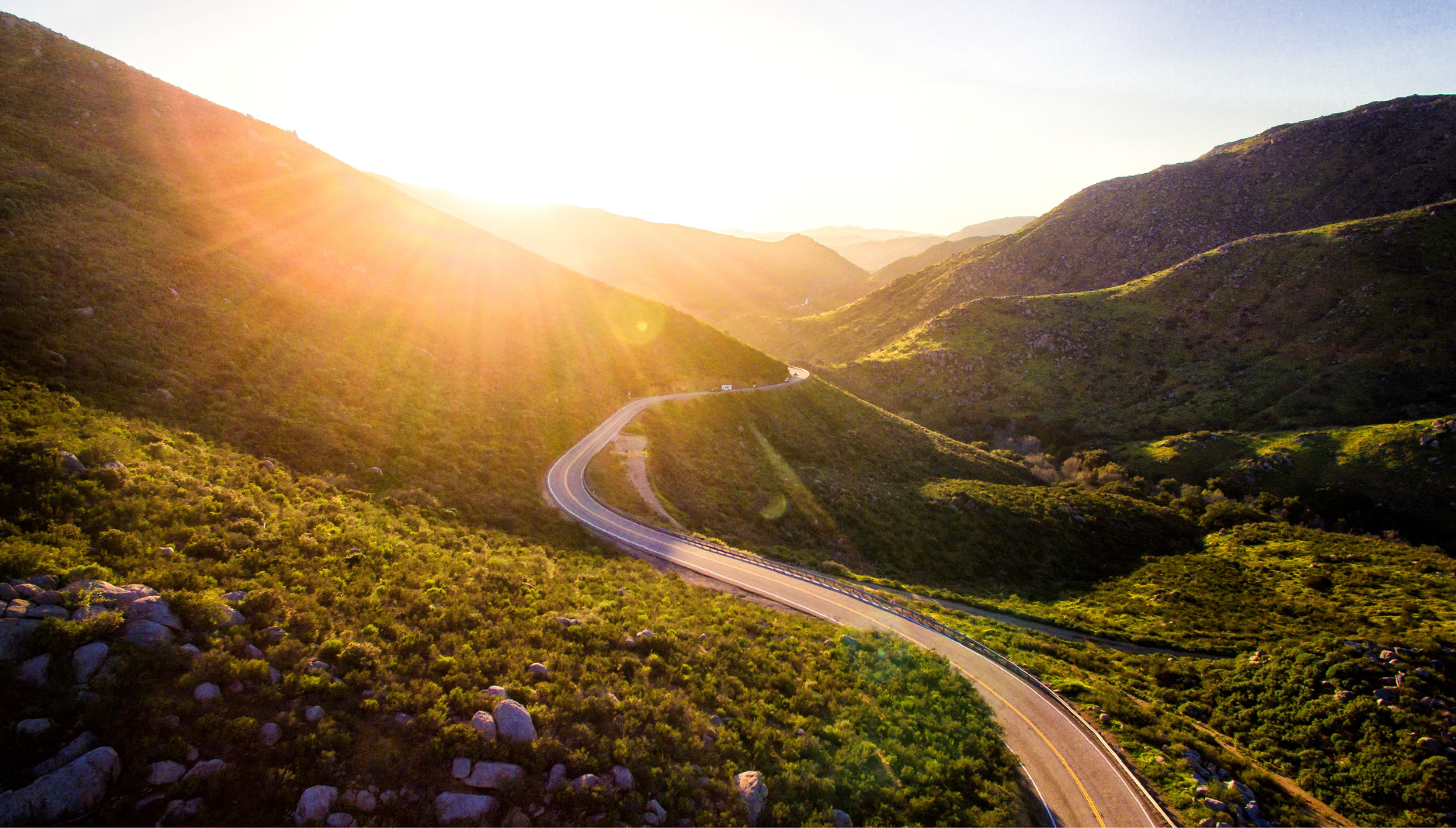 A pathway cutting through open hills toward the sunset.
